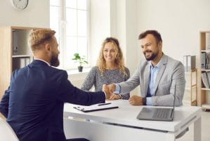 Happy couple shaking hands with real estate agent after signing contract at his office